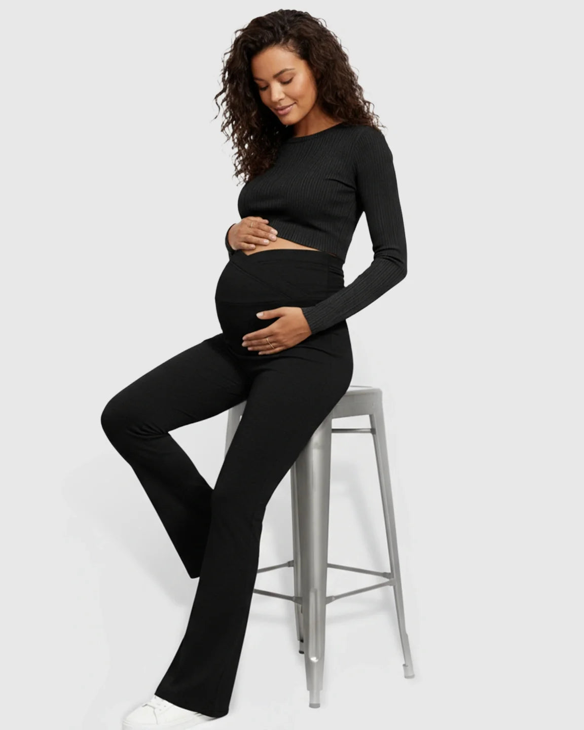 Pregnant woman in black ribbed long-sleeve crop top and black flared maternity pants with crossed waistband.