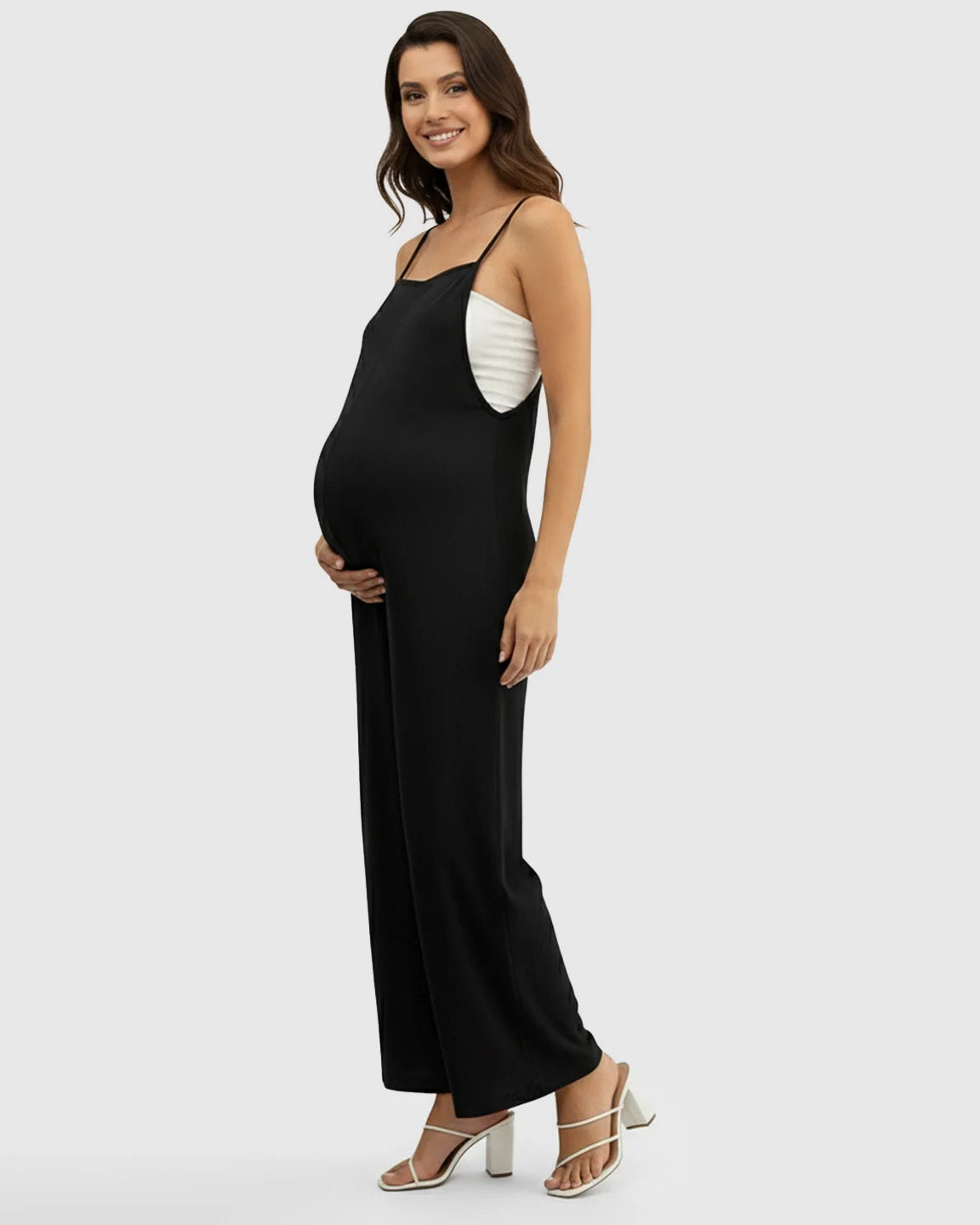 Smiling pregnant woman in a black spaghetti strap wide-leg maternity jumpsuit with a white top underneath.