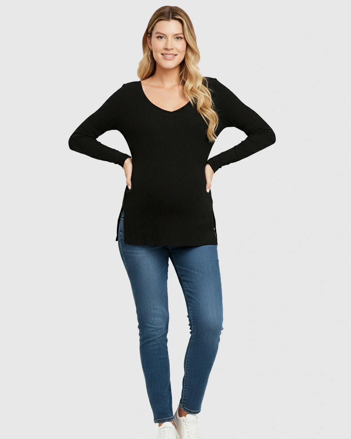 Smiling pregnant woman wearing a black ribbed V-neck long sleeve maternity top with side slits and jeans.