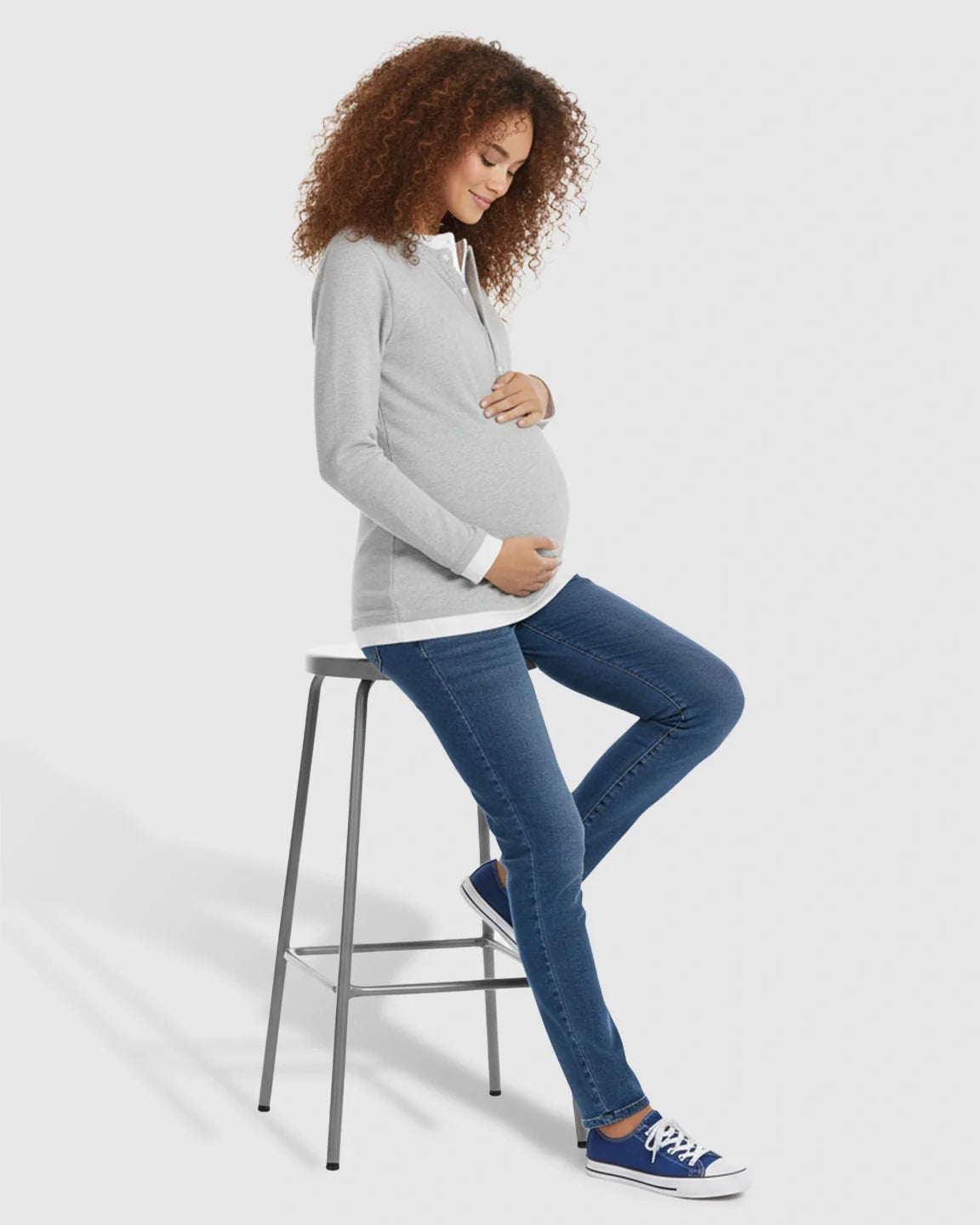 Pregnant woman in a gray button-front henley maternity and nursing top with white trim, blue jeans, and sneakers.