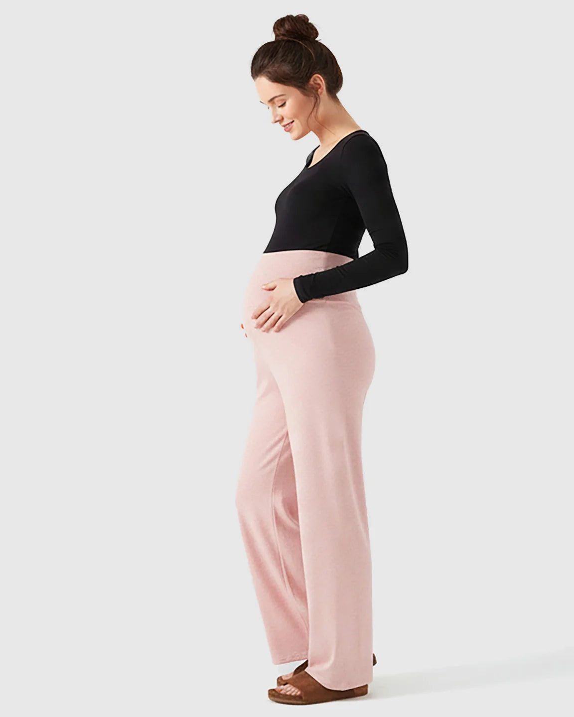 Smiling pregnant woman in pink fleece wide-leg maternity pants with over-belly waistband and black long-sleeve top.