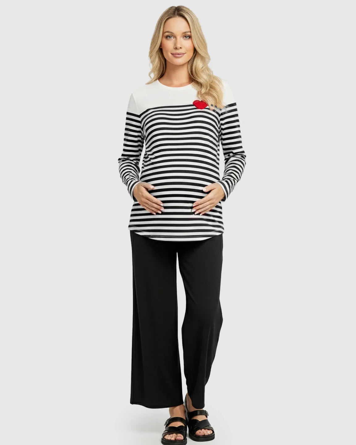 Woman wearing a black and white striped long-sleeve maternity top with a red heart and black wide-leg pants.