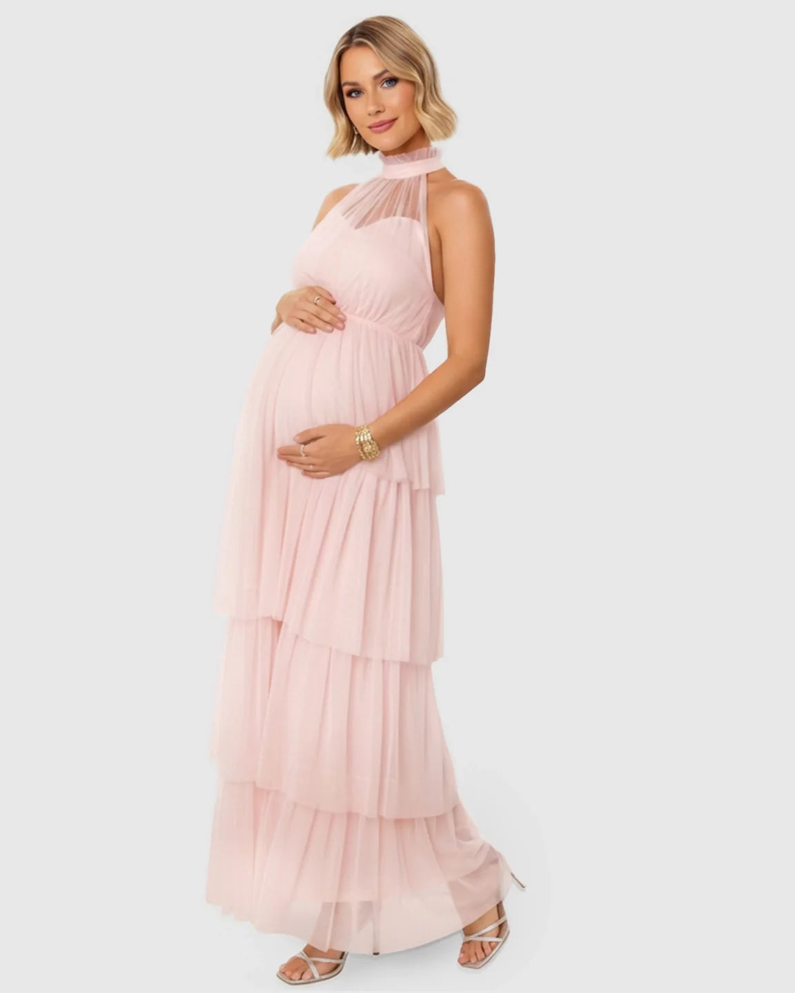 Pregnant woman in a pink halter neck tiered mesh maternity gown, holding her bump.