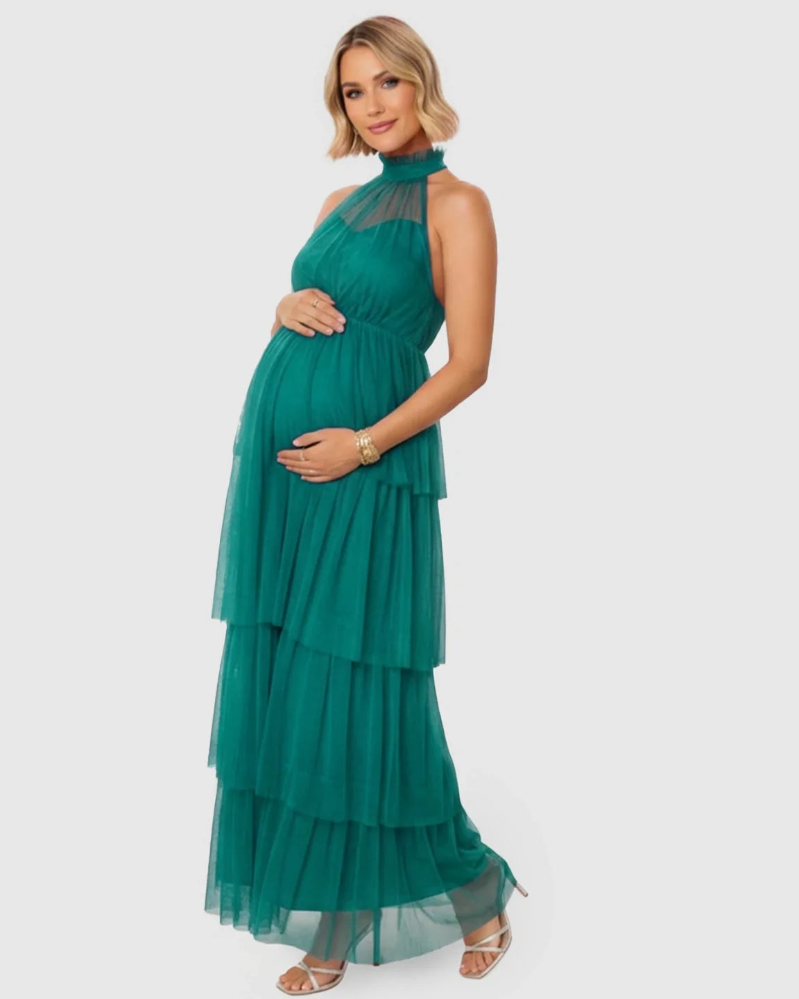 Pregnant woman in a green halter neck tiered mesh maternity gown, holding her bump.