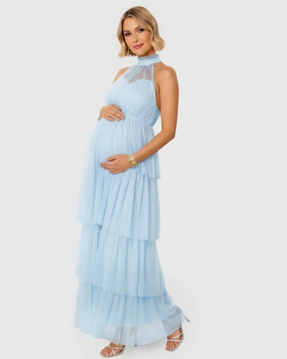 Maternity model in a light blue halter neck tiered mesh gown, cradling her bump.