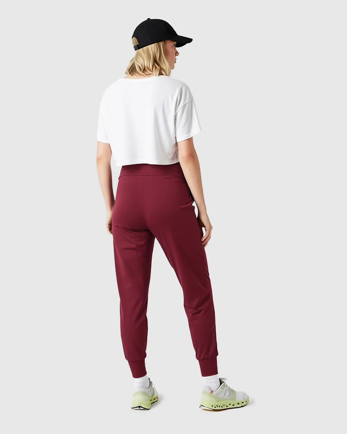 Woman from behind wearing supportive slim-fitting maroon maternity joggers, white crop top, and black cap.