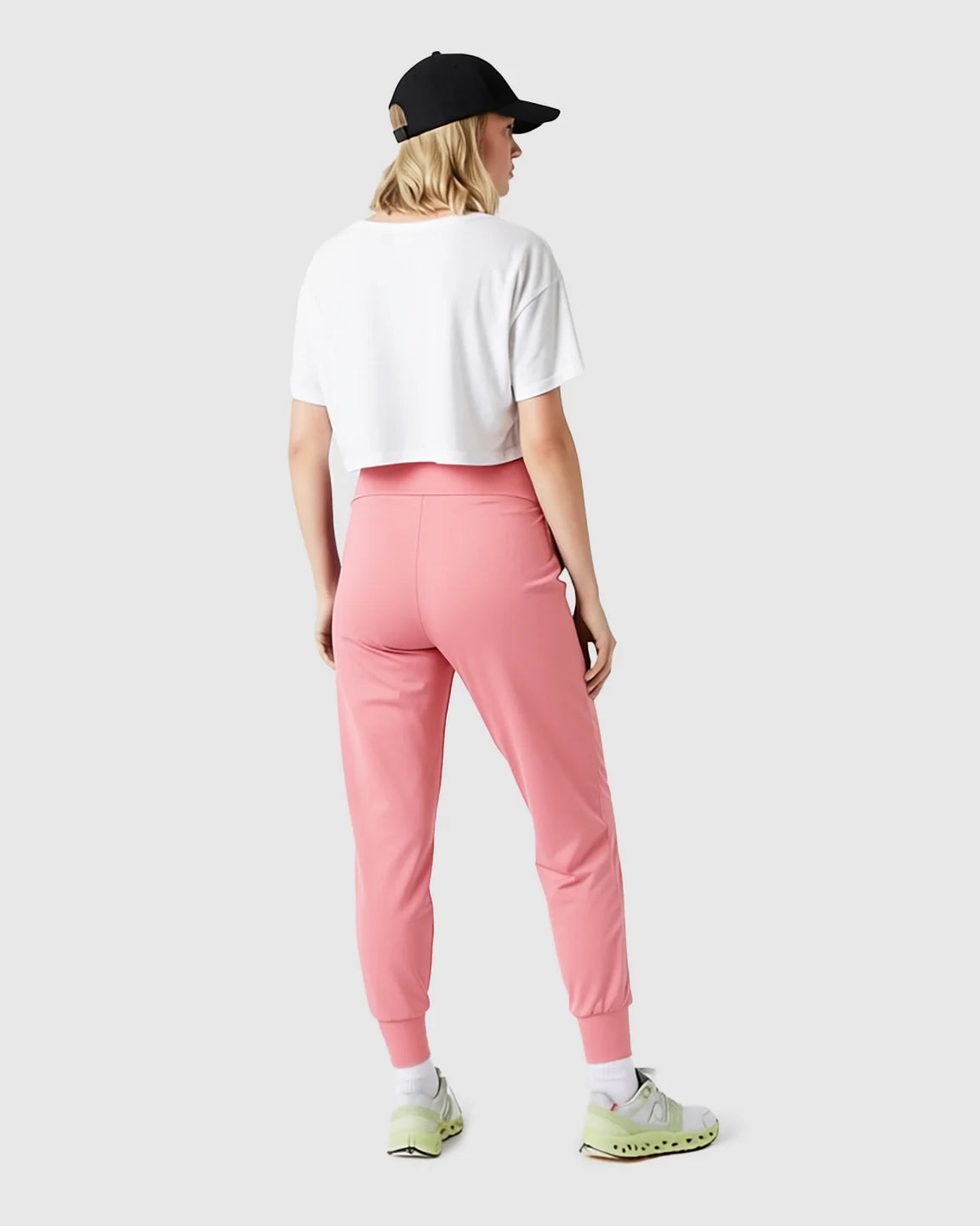 Woman from behind wearing pink supportive slim-fitting maternity joggers, a white crop top, and a black cap.