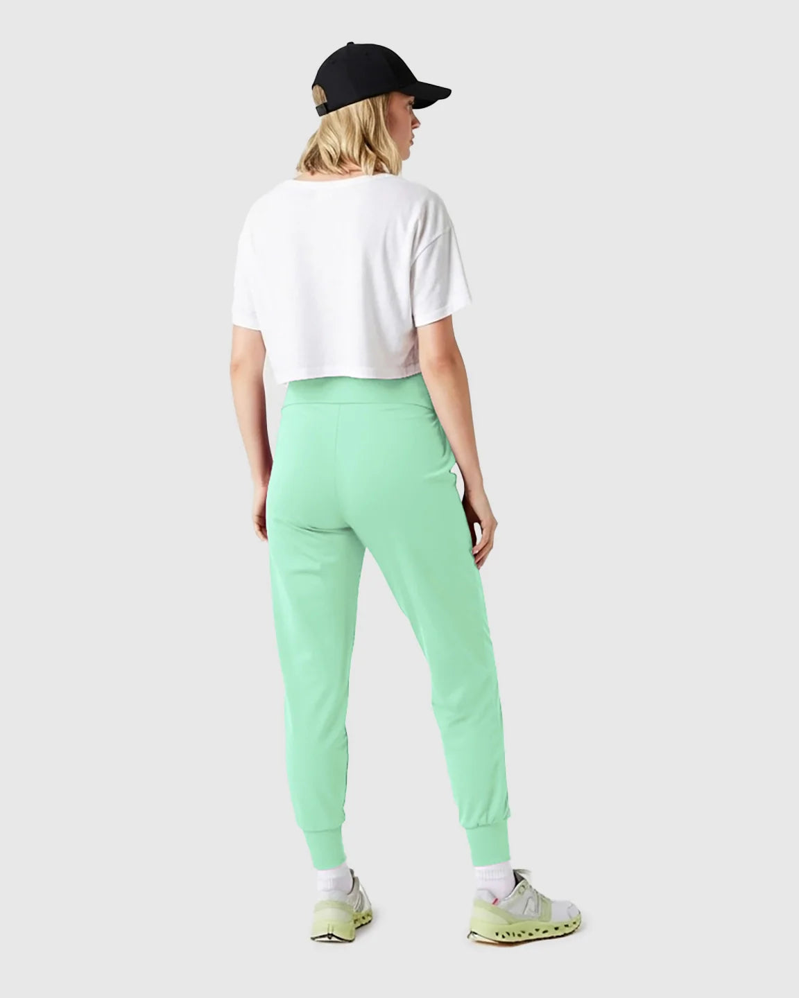Woman from behind wearing mint green supportive slim-fitting maternity joggers, white crop top, and black cap.