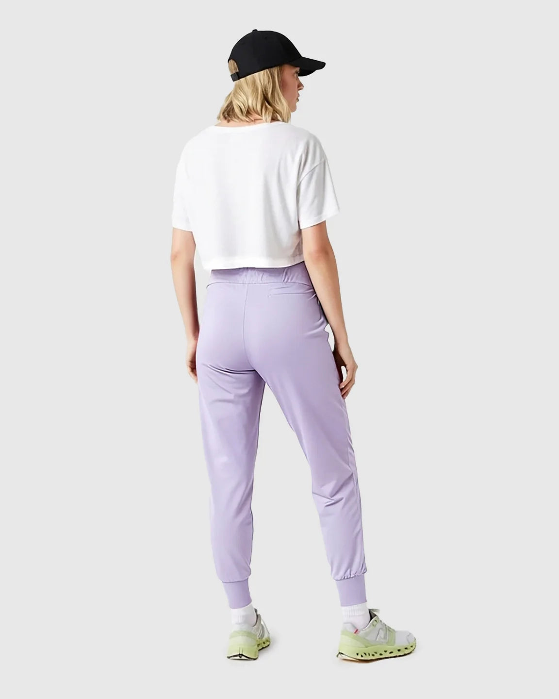 Woman from behind wearing lavender supportive slim-fitting maternity joggers, white crop top, and black cap.