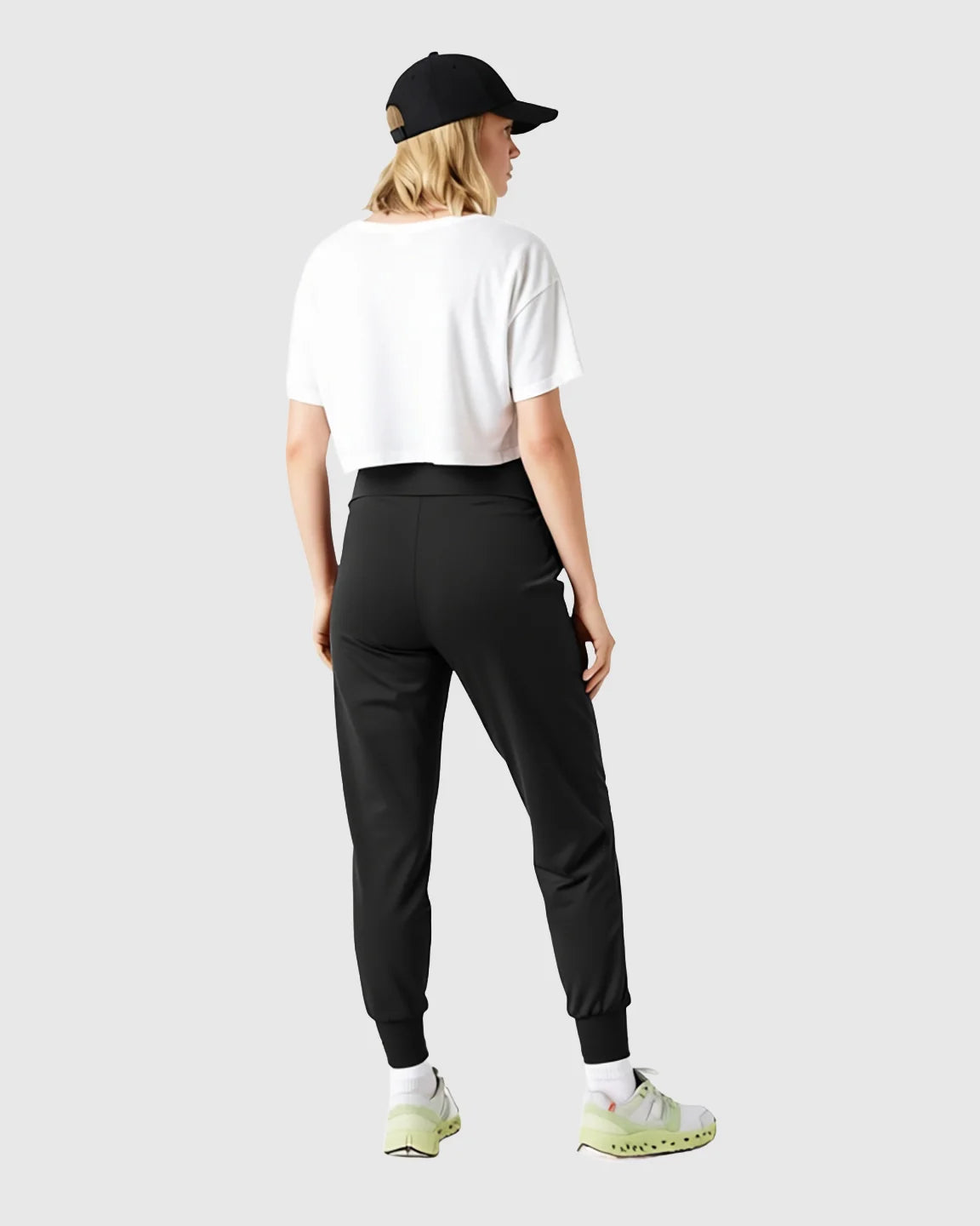 Woman from behind wearing black supportive slim-fitting maternity joggers, a white crop top, and a black baseball cap.