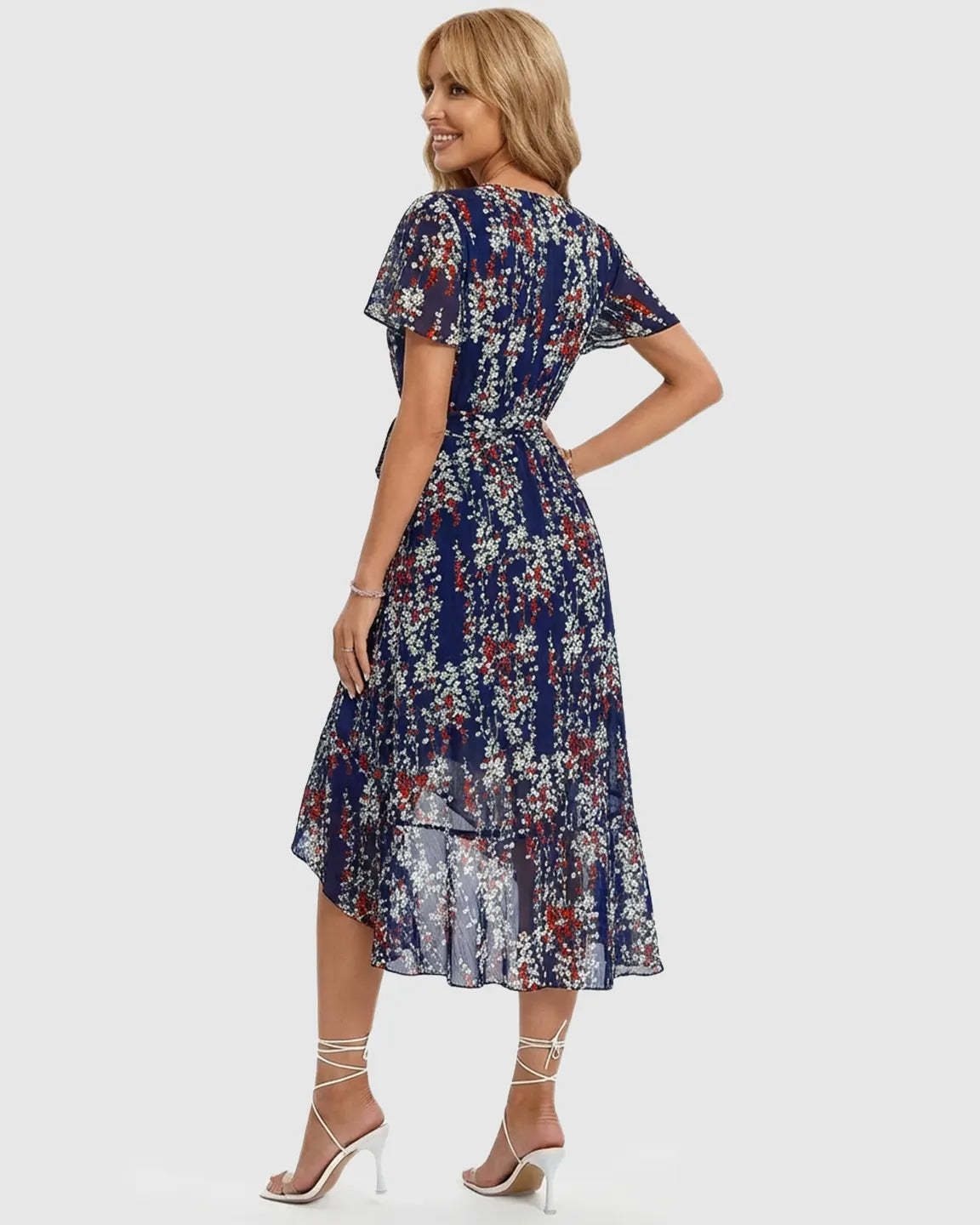 Smiling pregnant woman in a navy floral V-neck midi dress with ruffled hem and flutter sleeves.