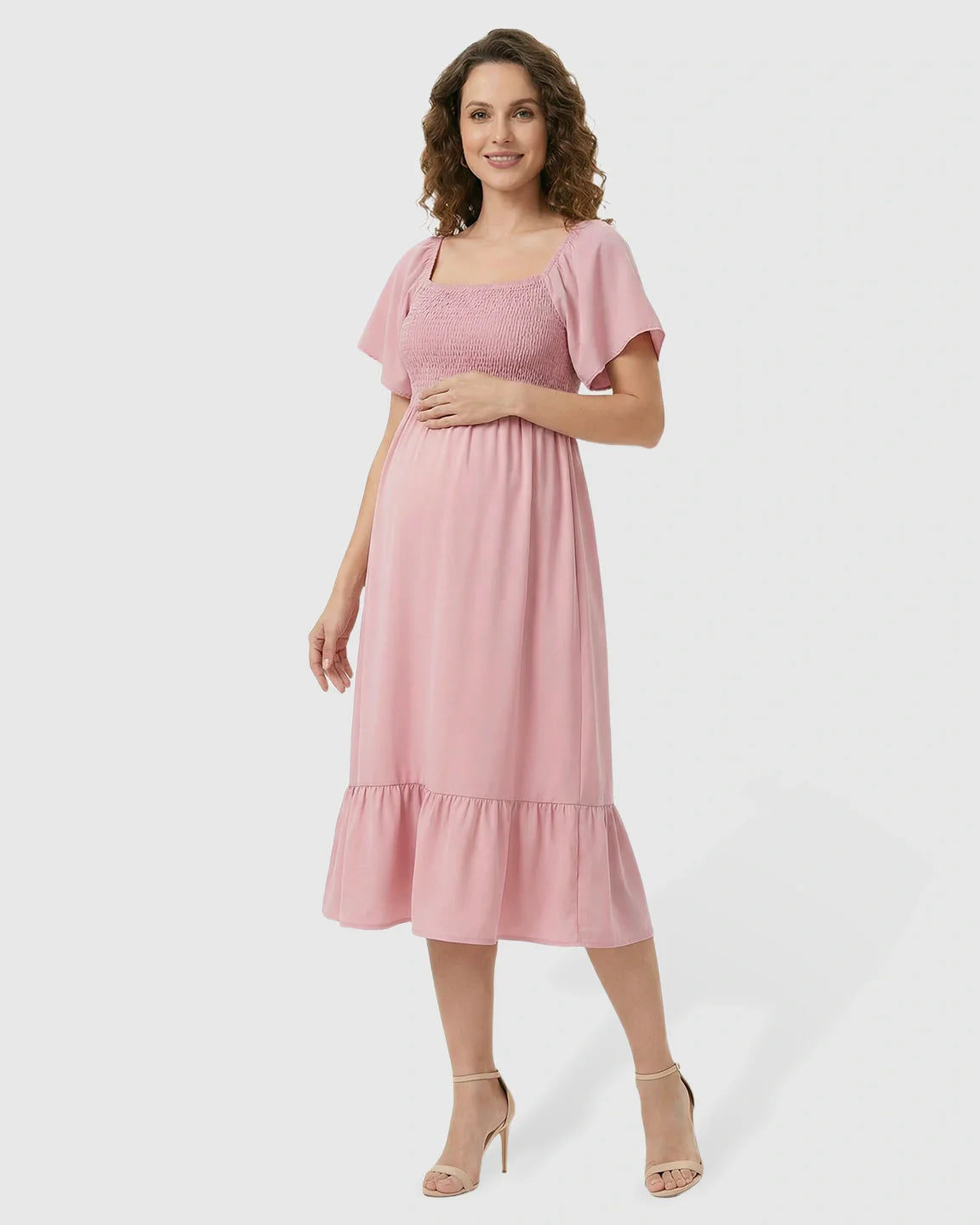 Smiling pregnant woman in a pink flutter-sleeve smocked maternity midi dress with a tiered skirt.