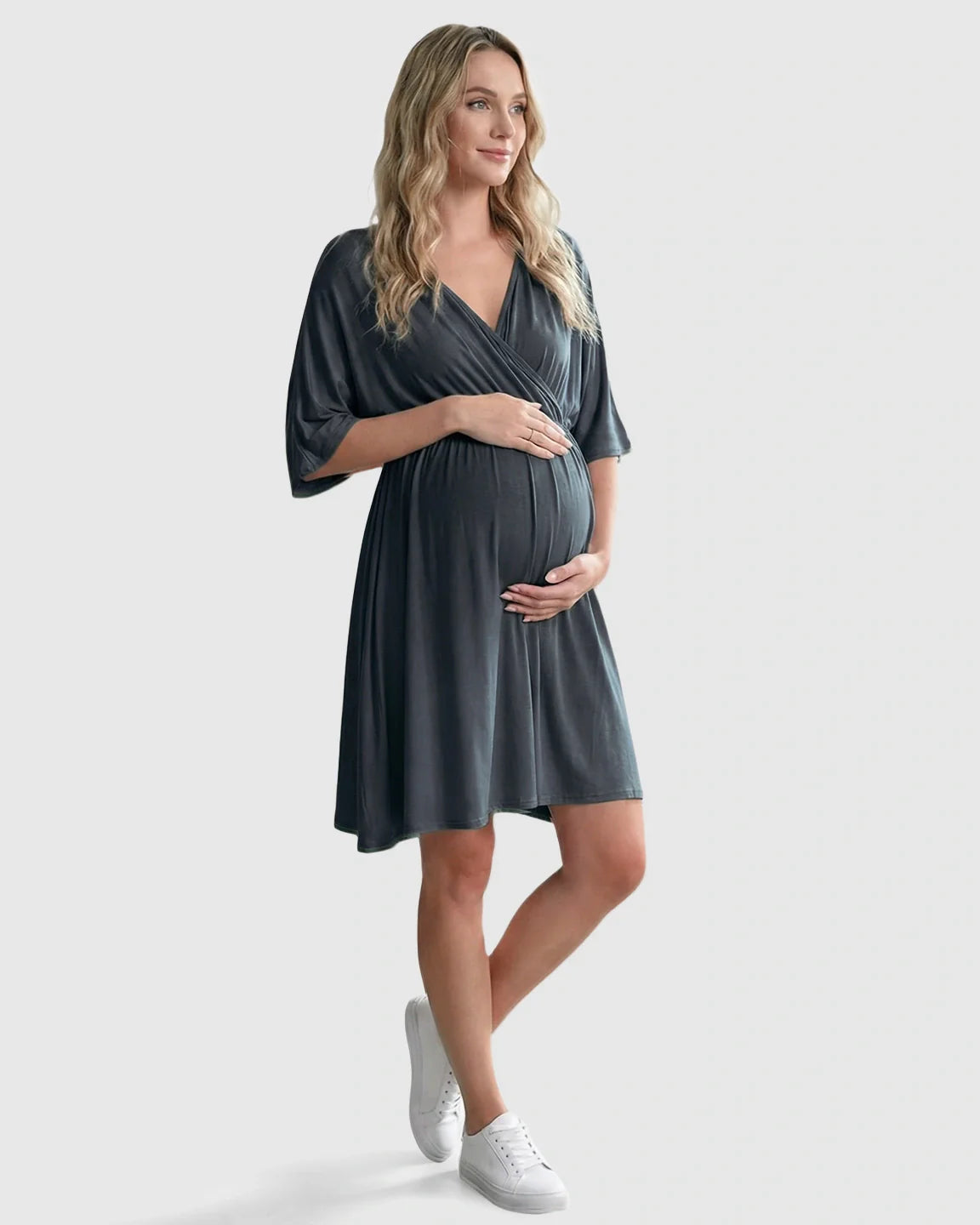Pregnant woman in a charcoal gray cross-front maternity midi dress with 3/4 sleeves, holding her bump.