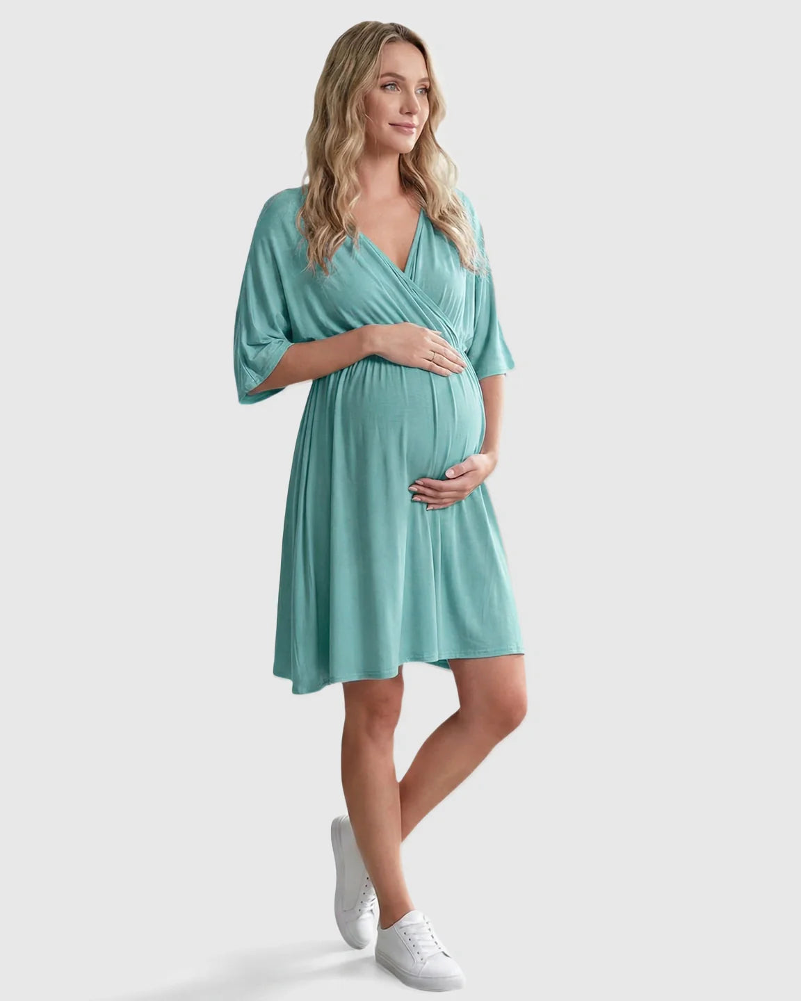 Pregnant woman in a teal cross-front maternity midi dress with 3/4 sleeves, holding her bump.