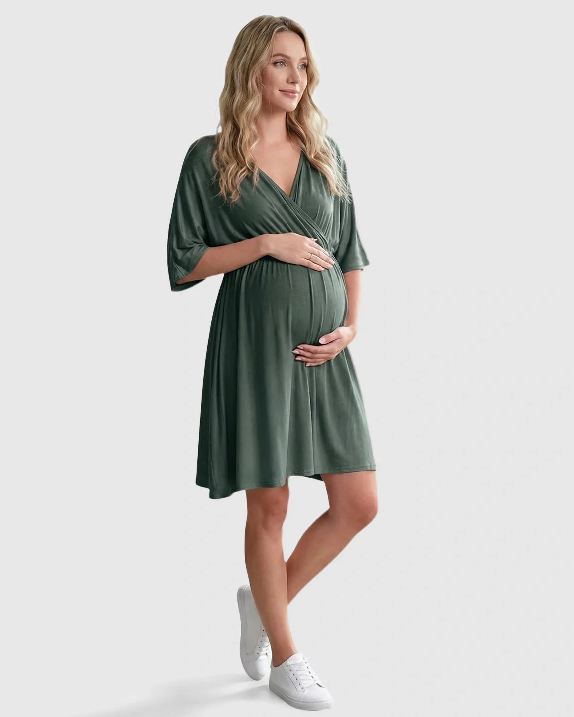 Pregnant woman in a soft, olive green cross-front maternity midi dress with 3/4 sleeves, holding her bump.