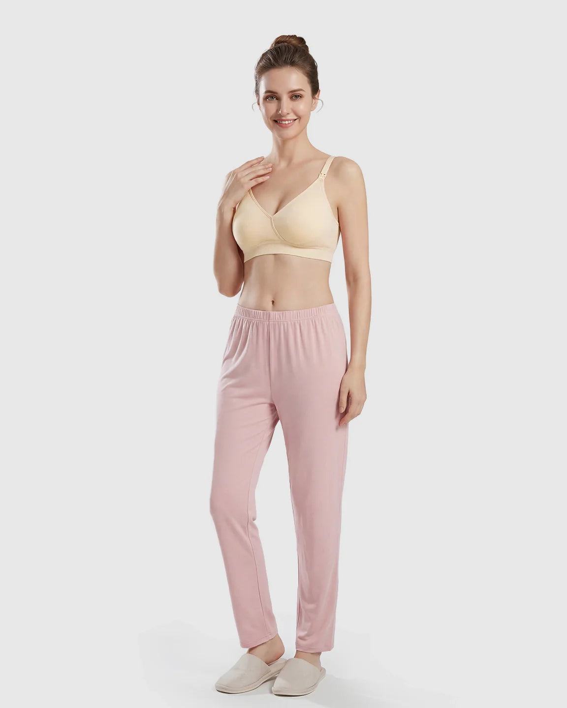 Smiling woman models a seamless, cross-front, wireless nursing bra in light yellow with pink pants.