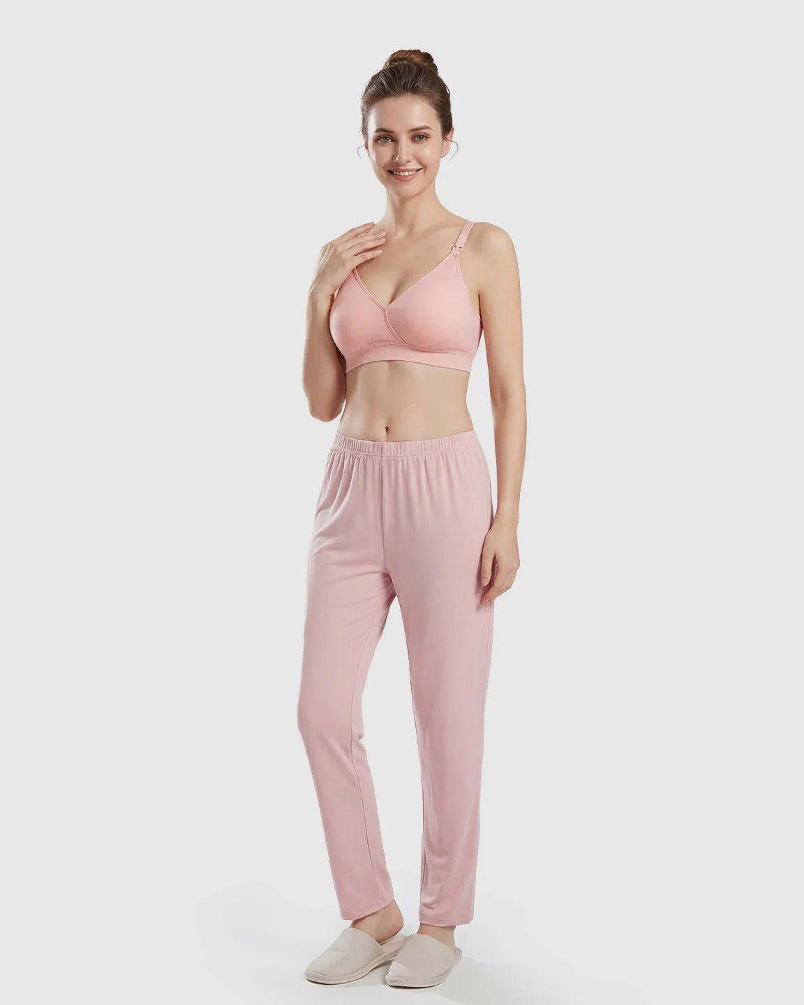 Smiling woman in a pink seamless cross-front wireless nursing bra and matching lounge pants.