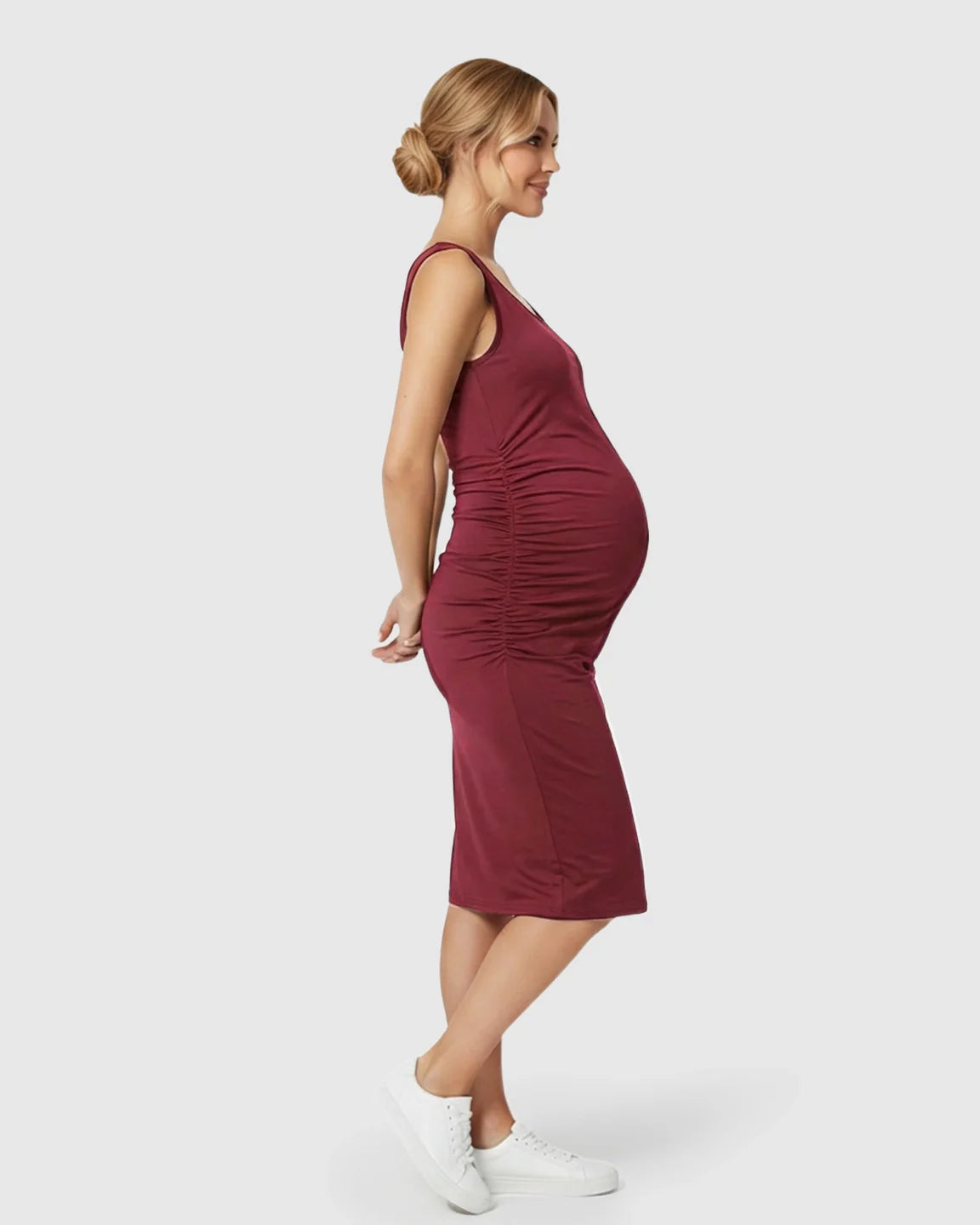 Smiling pregnant woman in a sleeveless, dark red bodycon maternity dress with side ruching.