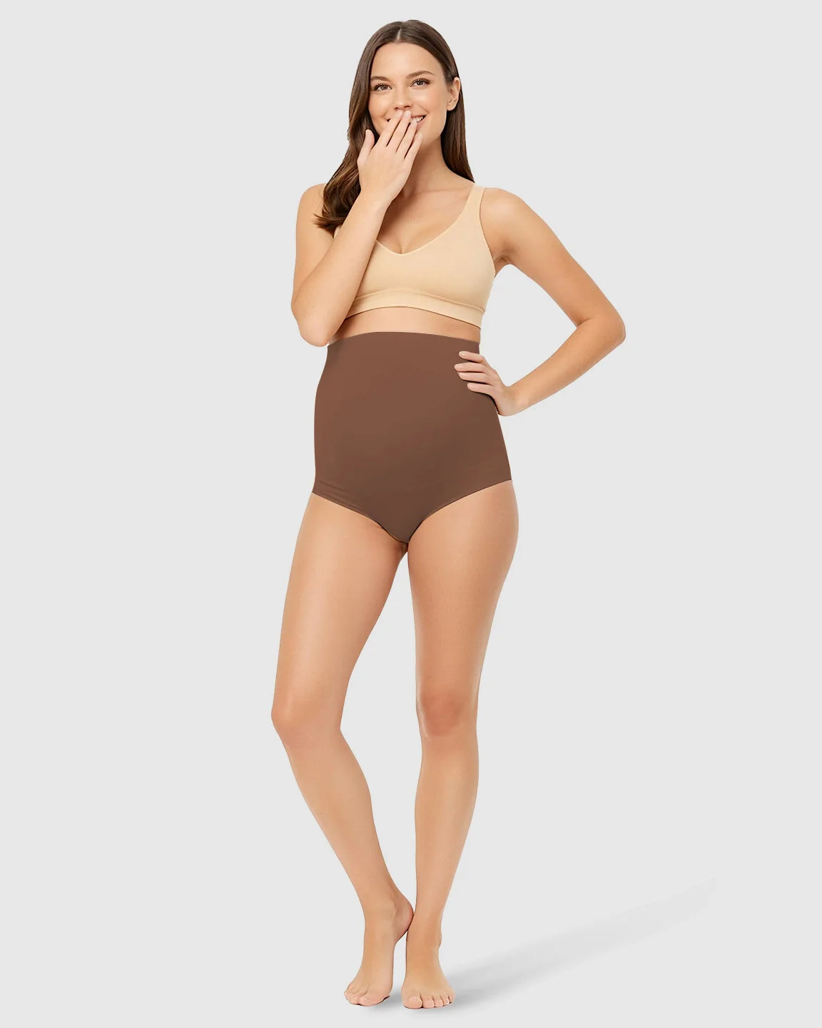 Smiling woman models brown high-waist seamless maternity underwear with belly support.