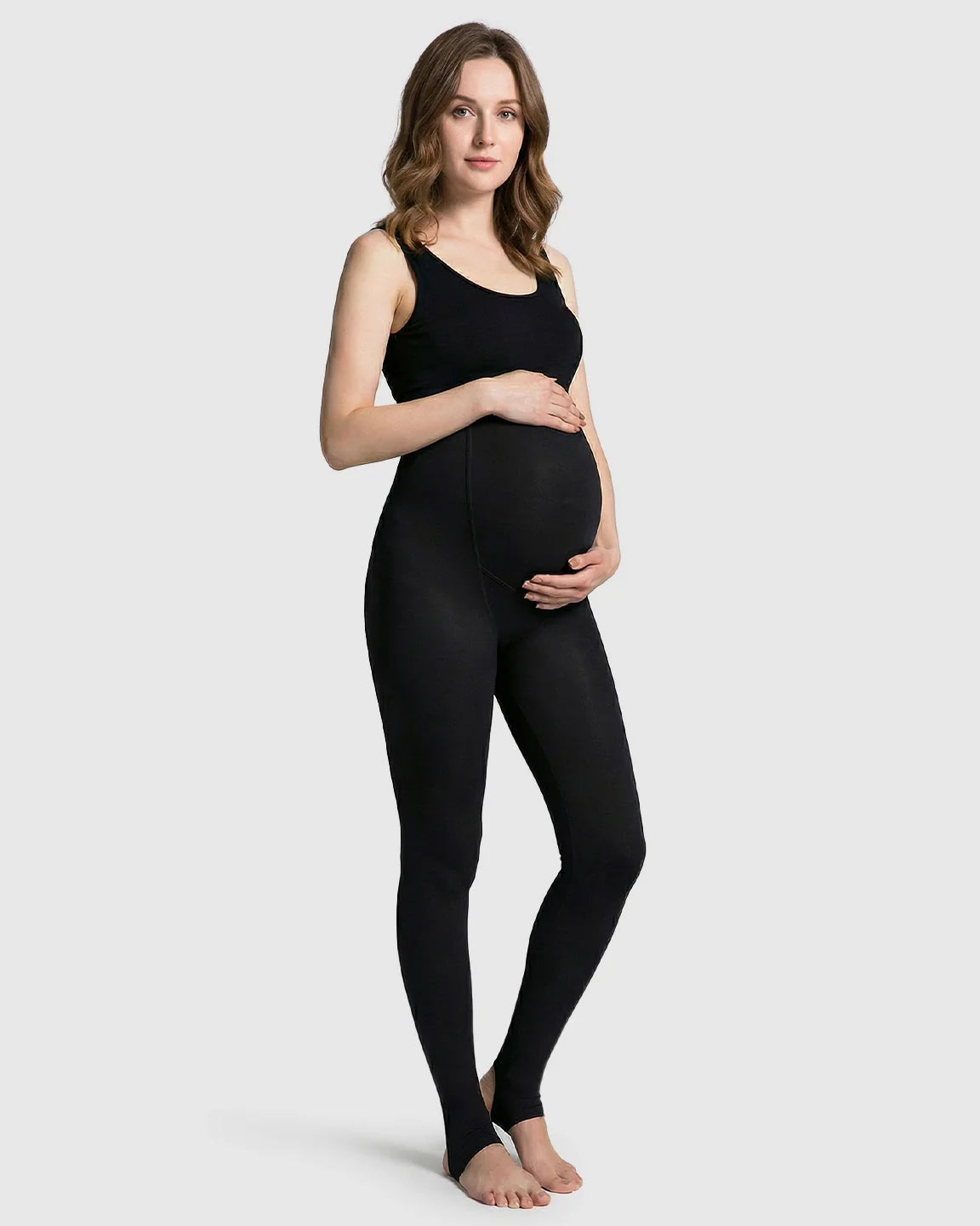 Pregnant woman in black fleece-lined over-bump maternity leggings with stirrups, holding her belly.