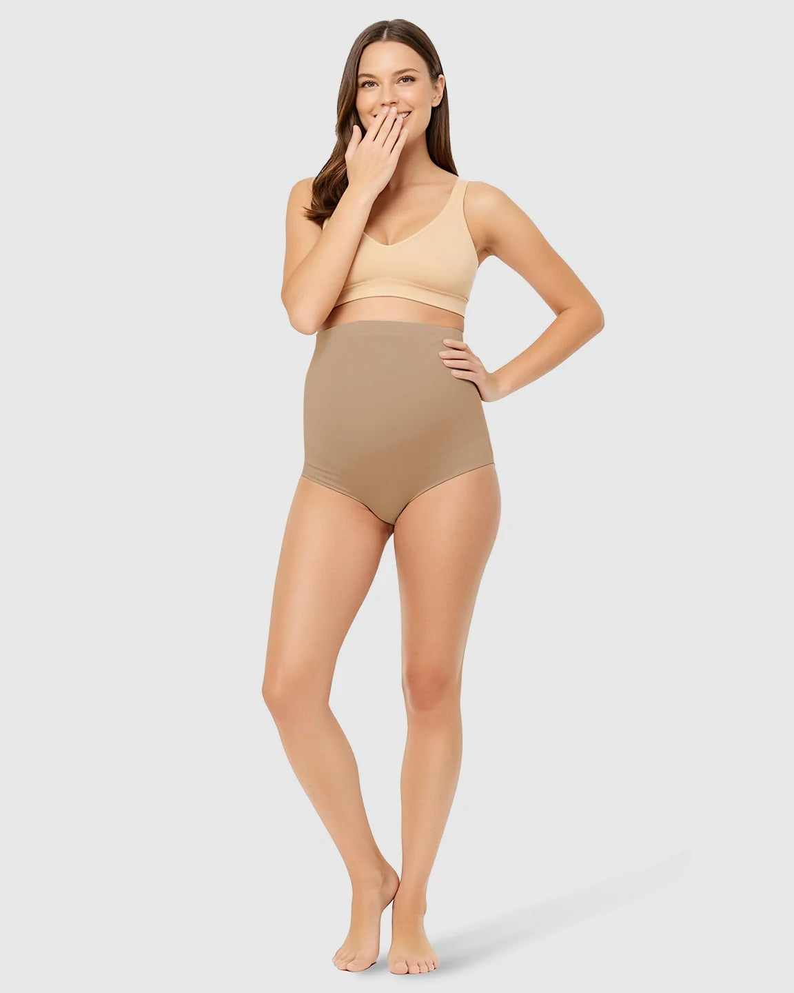 Smiling woman models Bump Society high-waist seamless maternity underwear in tan, offering belly support.