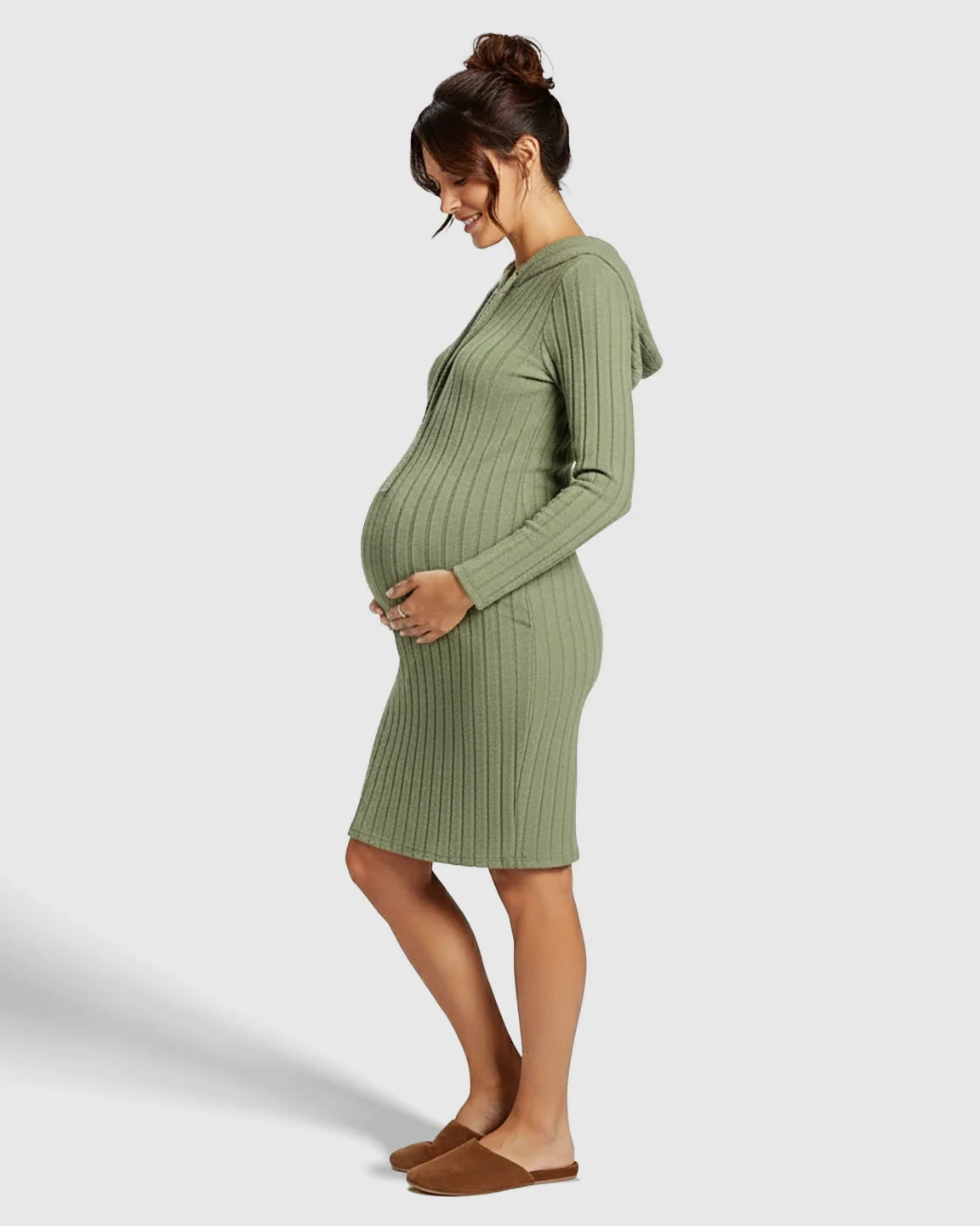 Pregnant woman in a sage green ribbed bodycon hooded maternity midi dress, gently cradling her bump.