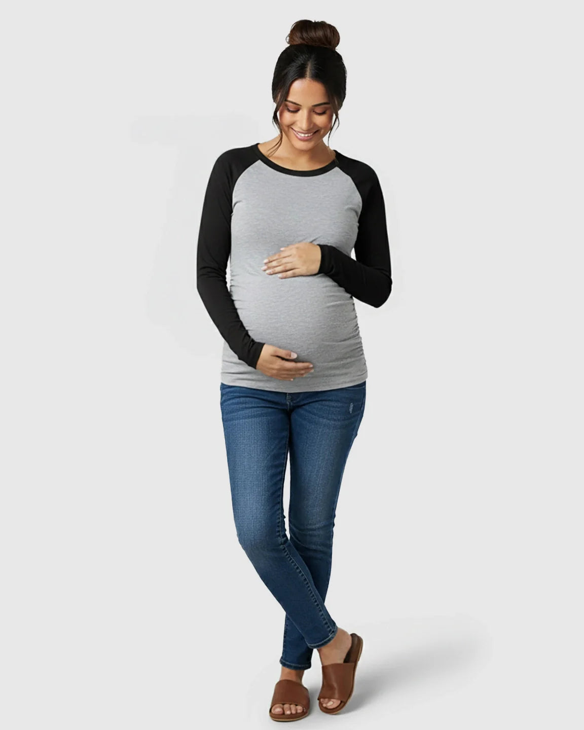 Smiling pregnant woman in a gray and black raglan sleeve maternity top with ruched sides and blue jeans.