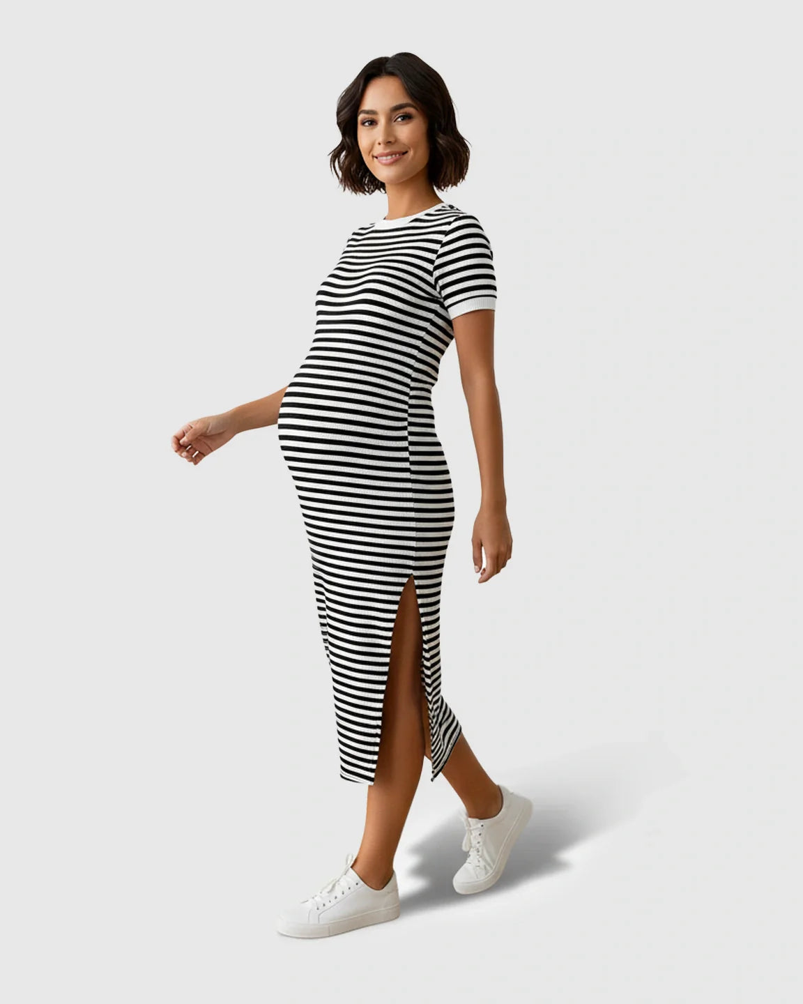 Smiling pregnant woman in a black and white striped maternity column dress with a side slit and white sneakers.