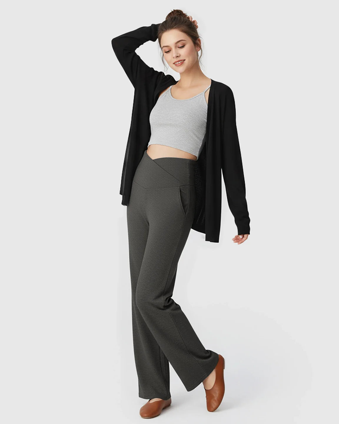 Woman in charcoal crossover waist wide-leg maternity lounge pants with pockets, grey crop top, and black cardigan.