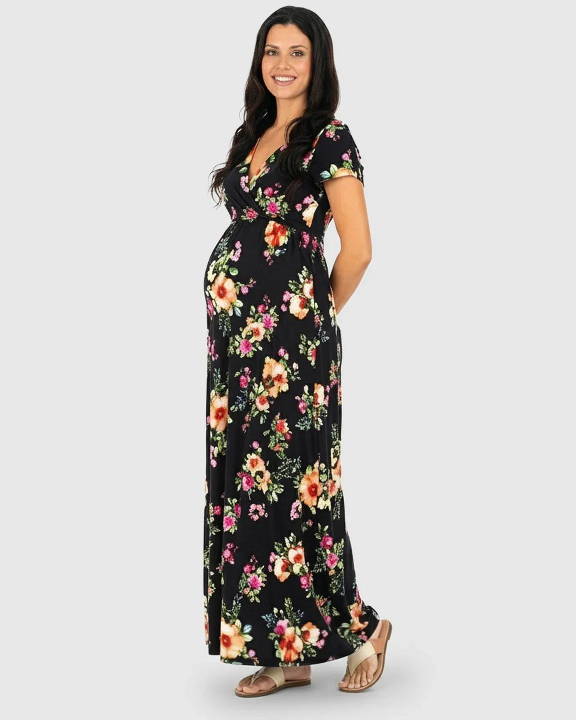 Smiling pregnant woman in a black floral V-neck short sleeve maternity maxi dress with sandals.