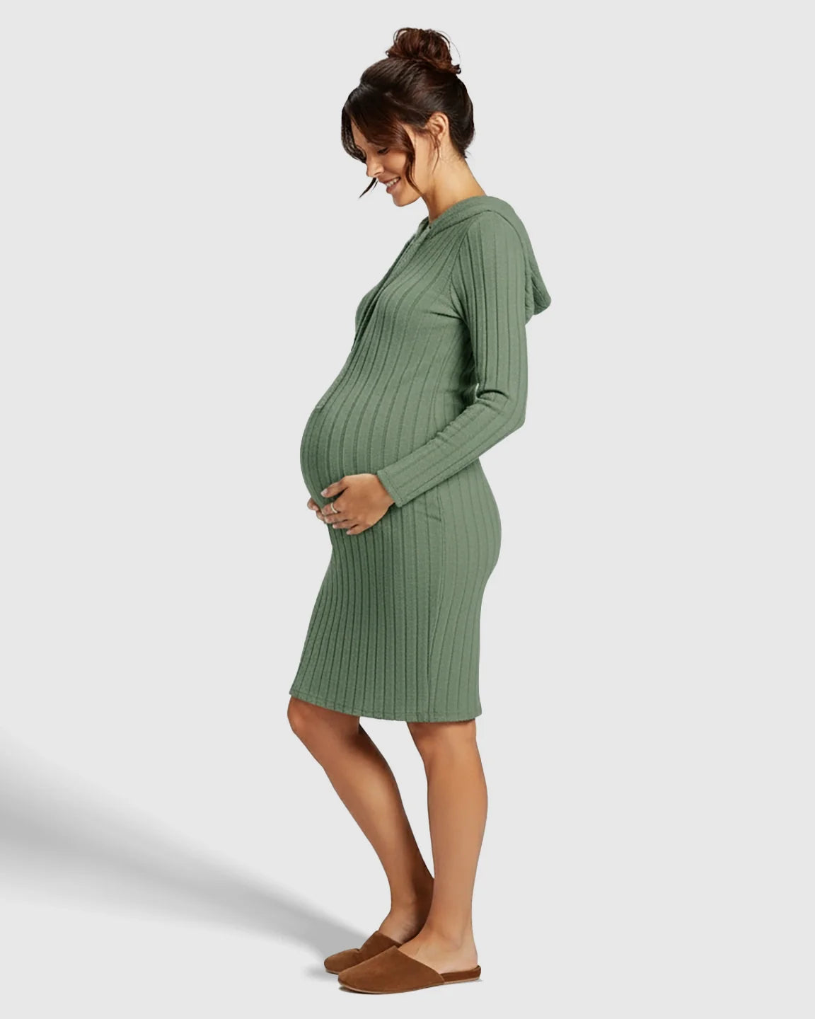 Pregnant woman in a green ribbed bodycon hooded maternity midi dress, gently holding her bump.