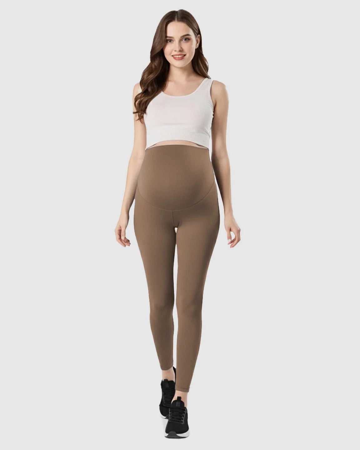 Smiling pregnant woman models brown double-layer belly support maternity leggings with a white crop top.