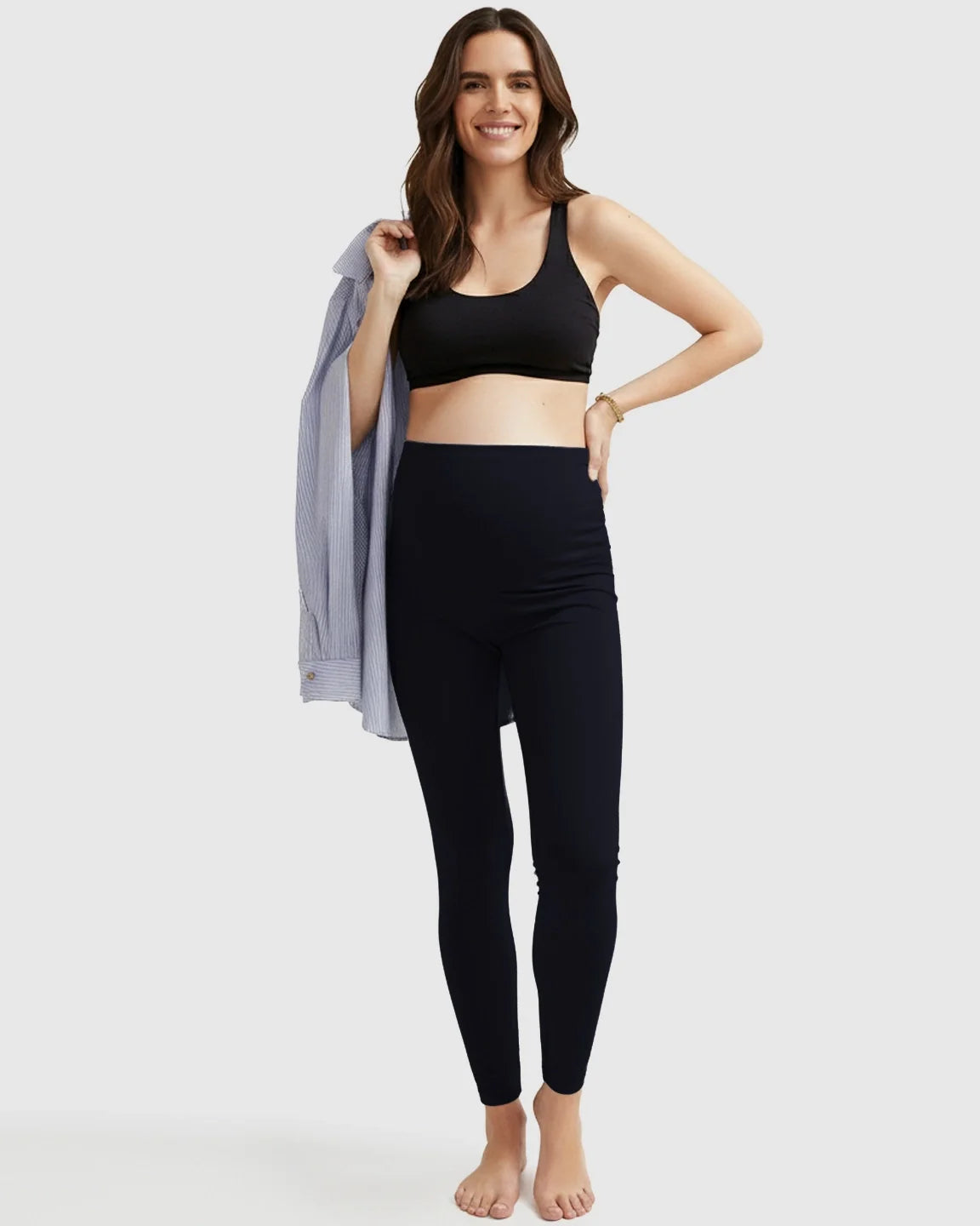 Smiling pregnant woman in black Bump Society ultra-soft support maternity midi leggings and a black bra.