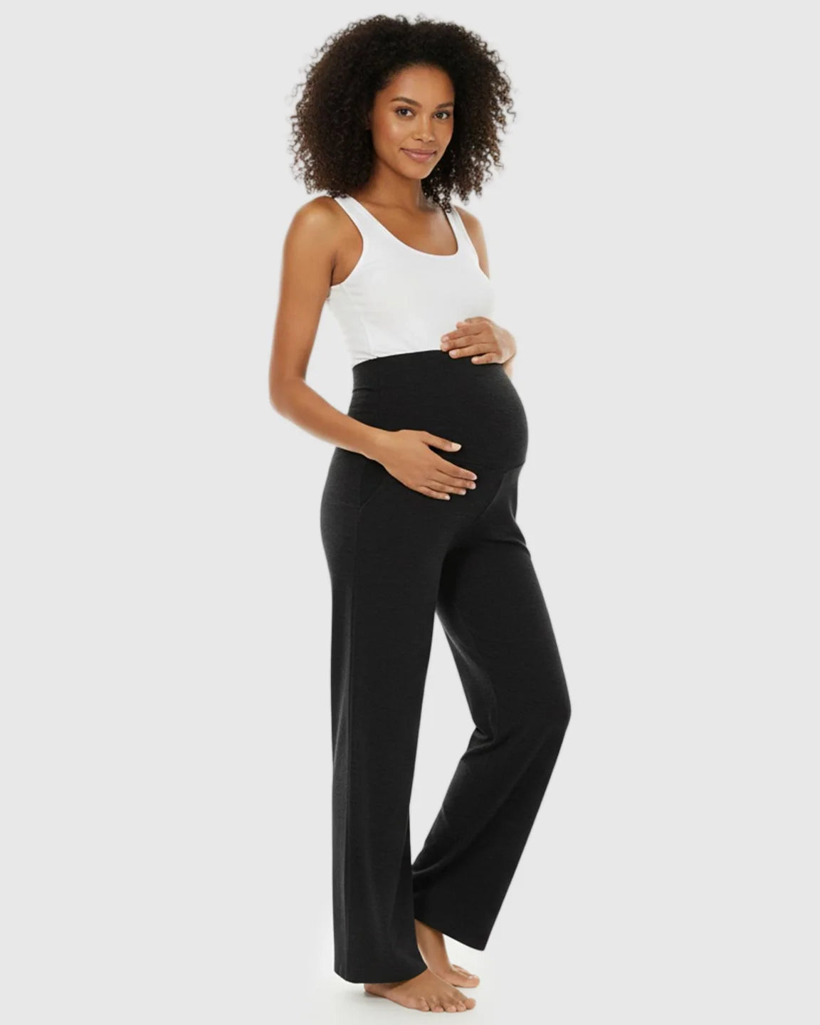Pregnant woman in black wide-leg maternity lounge pants with foldable waistband and white tank top.