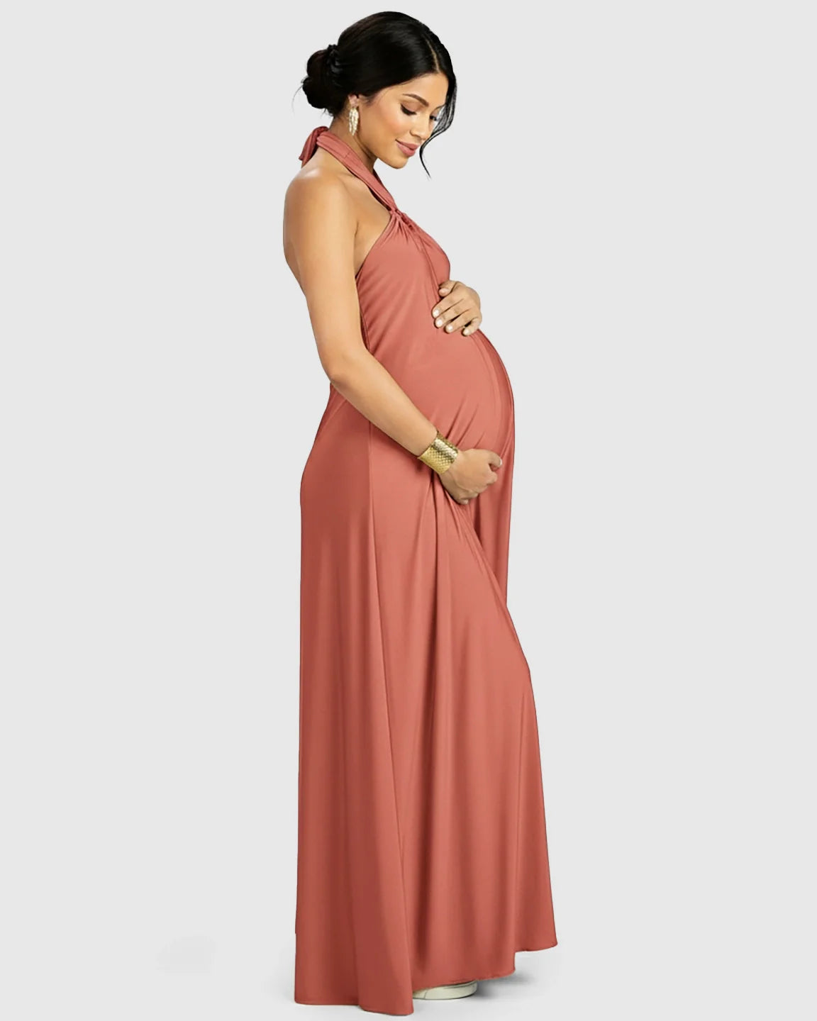 Pregnant woman in a terracotta backless halter neck chiffon maternity maxi dress, holding her bump.