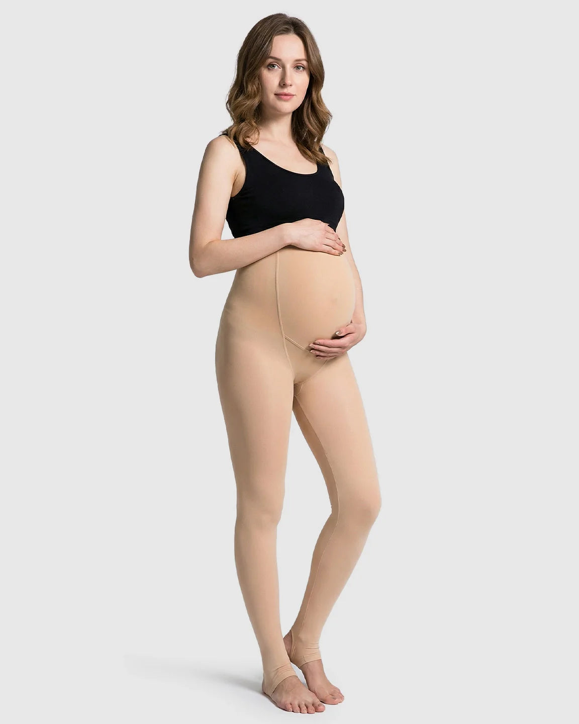 Pregnant woman modeling nude fleece-lined over-bump maternity leggings with stirrups, paired with a black tank top.