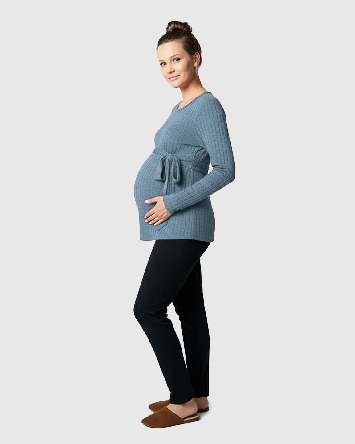 Pregnant woman in a blue ribbed tie-waist long sleeve maternity sweater and black pants.