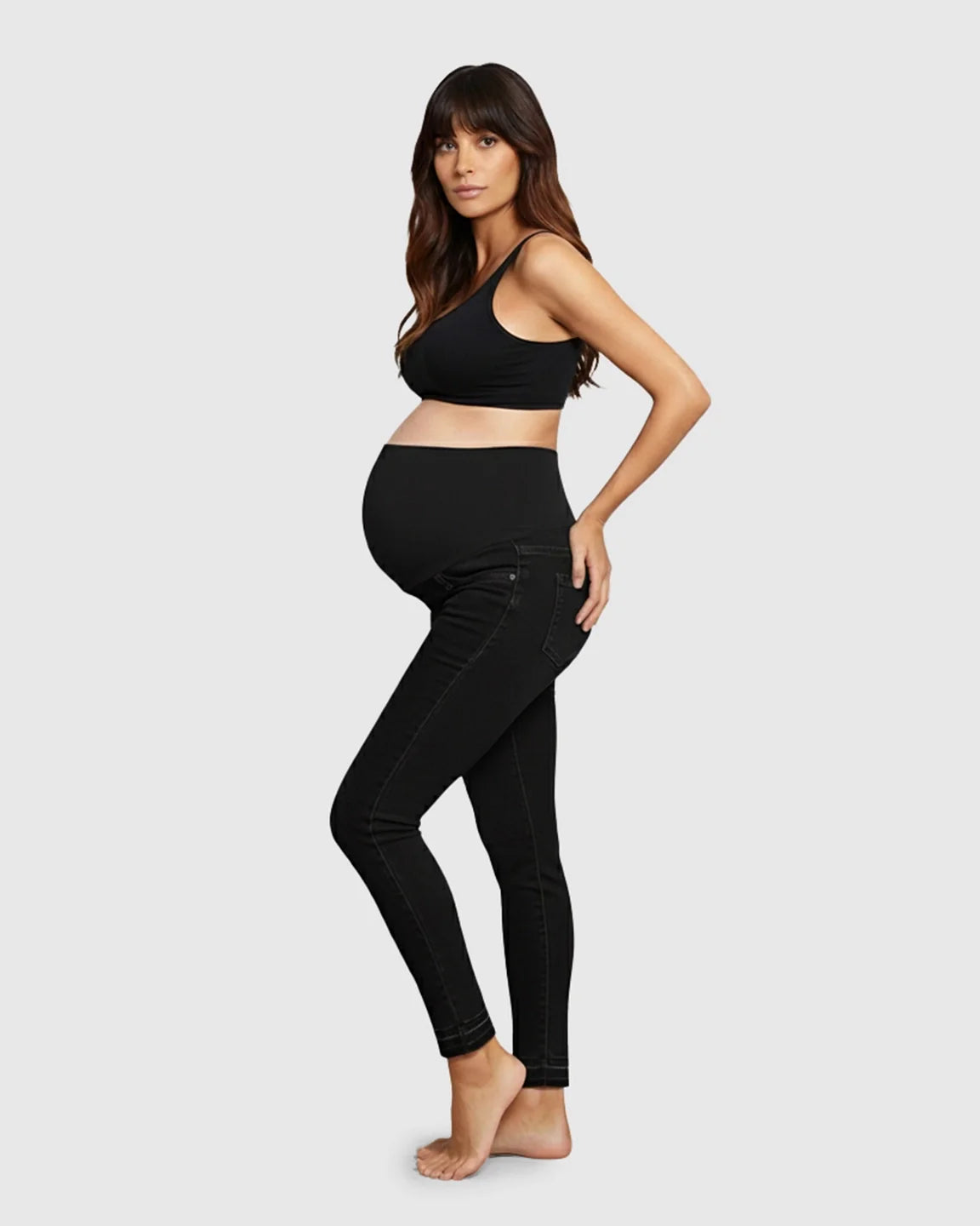 Pregnant woman in black high-waist skinny maternity jeans with an elastic waistband and black bra.