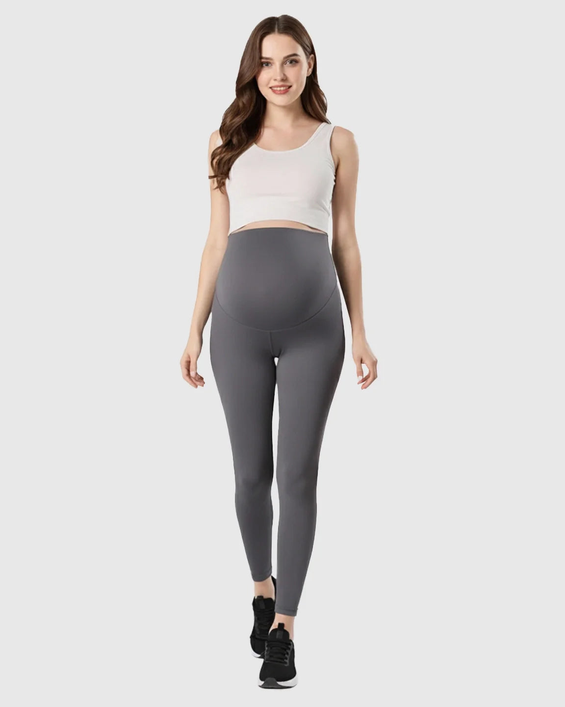 Smiling pregnant woman in gray double-layer belly support maternity leggings and a white crop top.