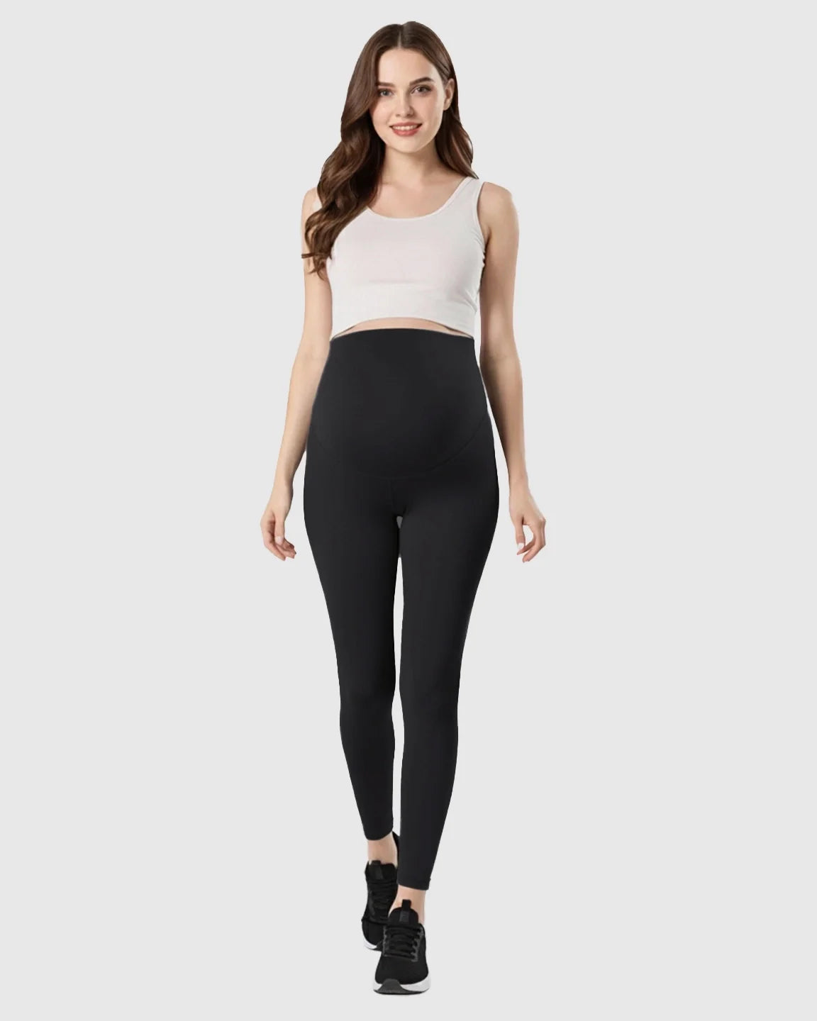 Smiling pregnant woman wearing black double-layer belly support maternity leggings and a white crop top.