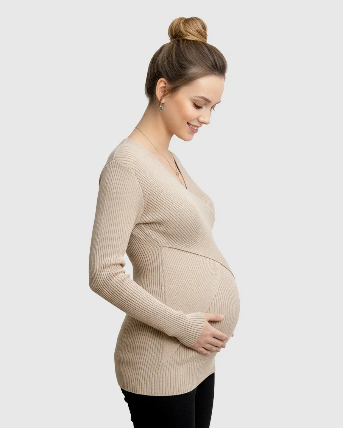 Smiling pregnant woman in a beige ribbed faux-wrap maternity top, cradling her bump.
