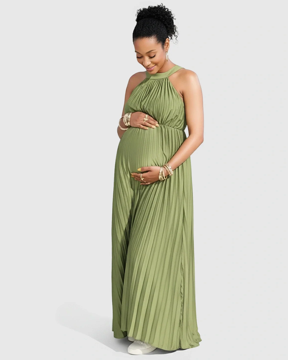 Pregnant woman in a sage green faux silk halter neck pleated maternity maxi dress, gently cradling her belly.
