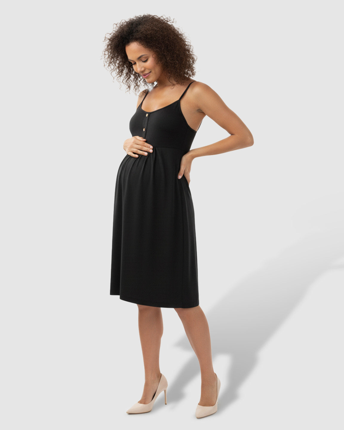 Pregnant woman in a black A-line maternity midi dress with thin straps, holding her bump.
