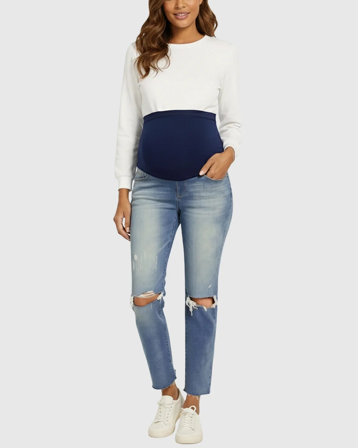 Smiling pregnant woman in distressed light wash maternity jeans with a navy belly band and white top.