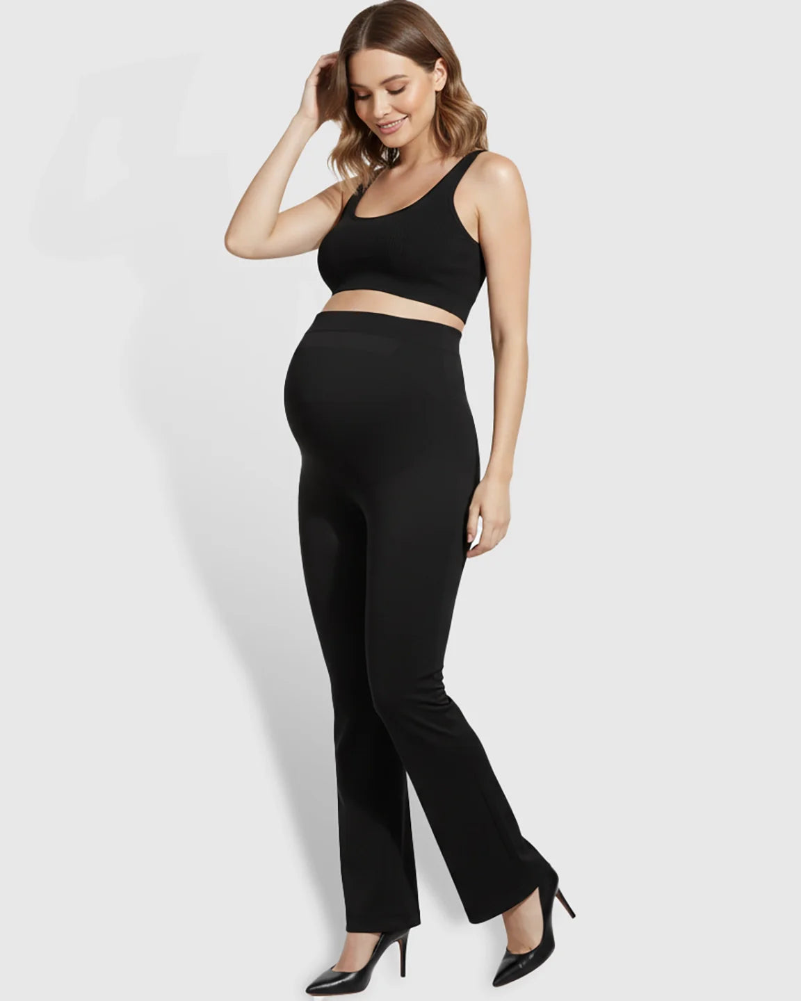 Smiling pregnant woman in black over-belly bootcut maternity pants and a matching crop top.