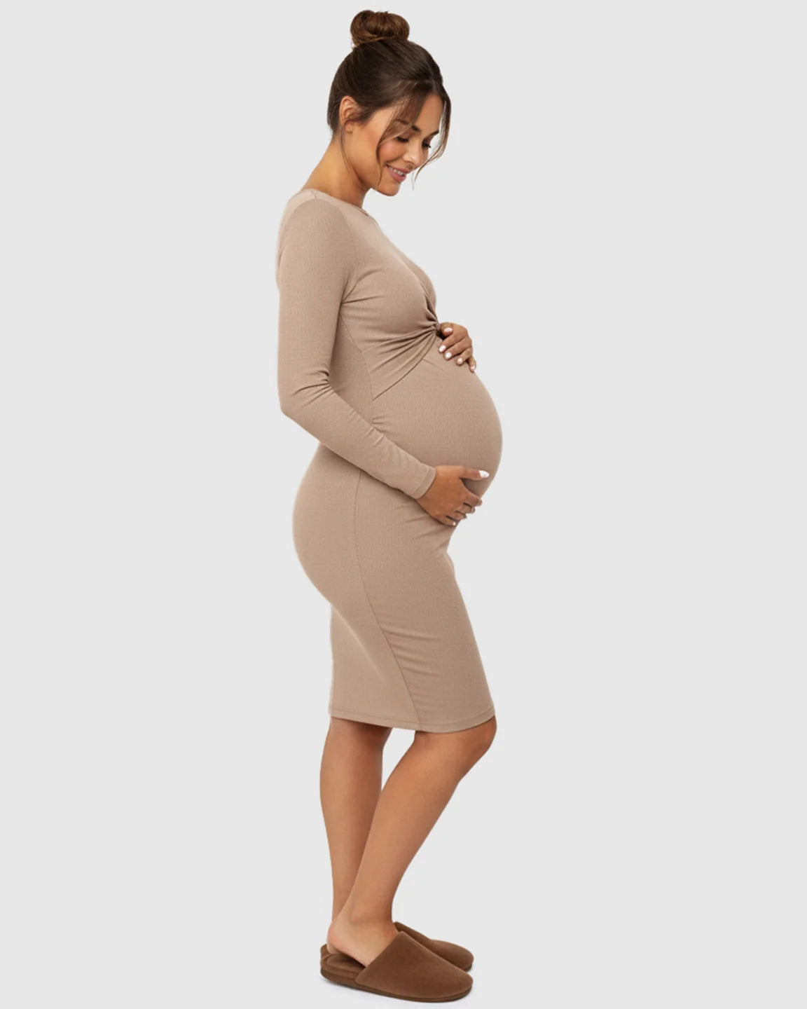 Pregnant woman in a beige ribbed bodycon maternity dress with a twist-front detail, smiling.