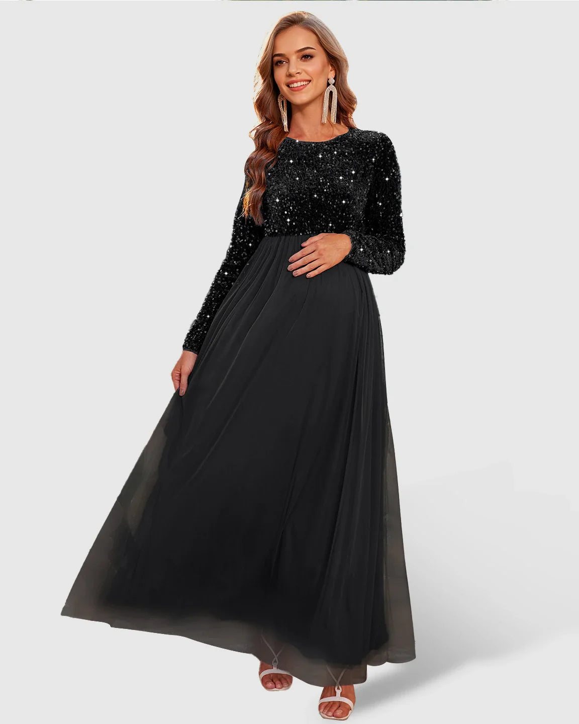 Smiling pregnant woman in a black sequin long-sleeve empire waist maternity maxi dress with a flowing mesh skirt.