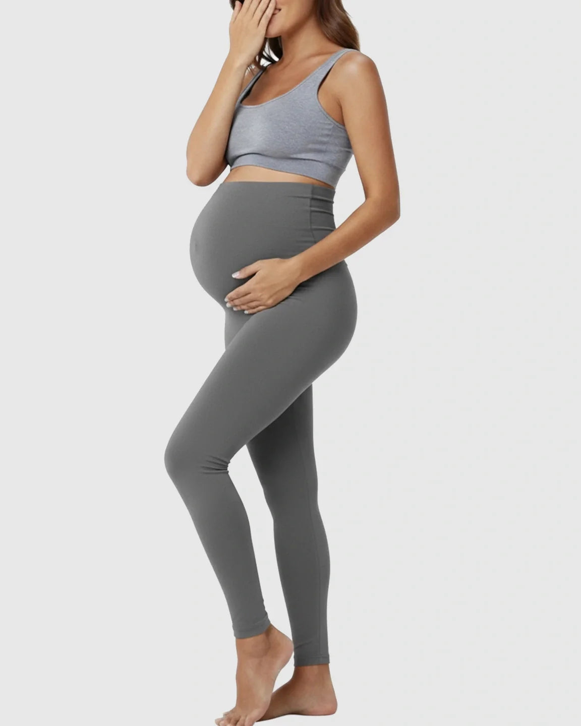 Pregnant woman in full-length, seamless charcoal grey high-waist maternity support leggings and a grey bra top.