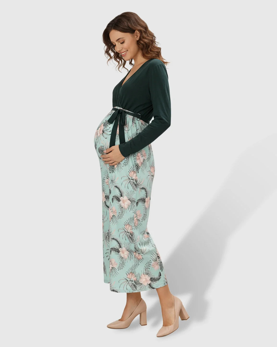 Pregnant woman in a long-sleeve V-neck deep green and floral print maternity midi dress with a tie waist.