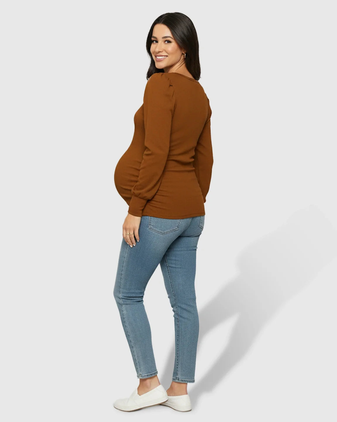 Smiling pregnant woman in a warm brown long-sleeve ruched maternity top and blue jeans.